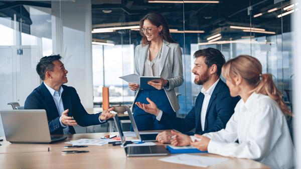 business meeting with four professionals discussing ideas while looking at documents and laptops focused on teamwork and collaboration in a modern office setting