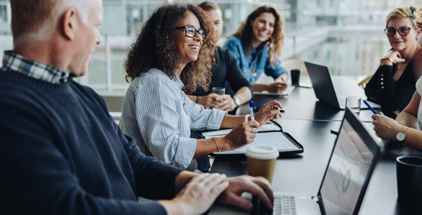 diverse group of professionals engaged in a meeting at a conference table with laptops and coffee discussing ideas in a collaborative setting