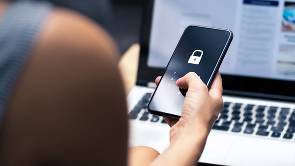 person using a smartphone with a lock screen in front of a laptop focused on online security measures